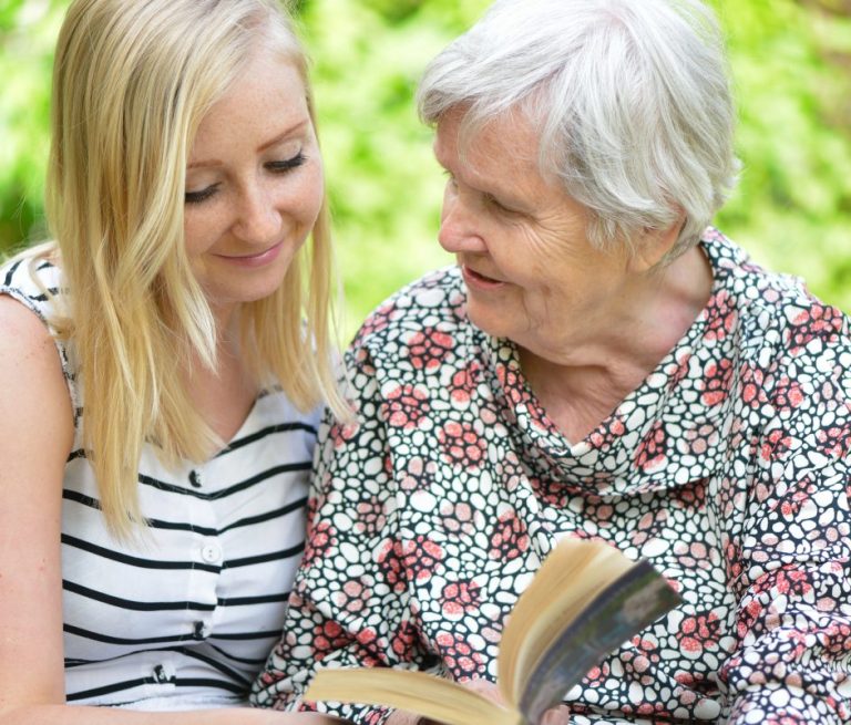 Oma hält Buch in der Gedichtband in der Hand und Tochter schaut in das Buch.