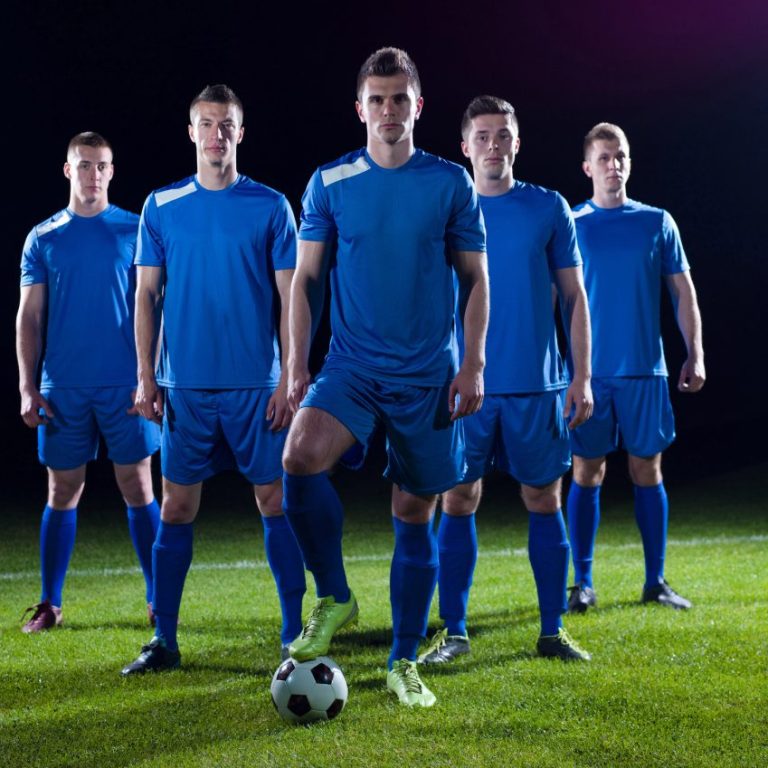 Andreas Bertram Auftragsgedicht Verein Fußball Fünf Fußballspieler in blauen Trikots stehen zu den Seiten nach hinten versetzt. Der Mittlere ist hält seinen Schuh auf dem Ball.